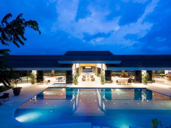 A luxurious modern building with a large illuminated swimming pool in front, set against a dusk sky.