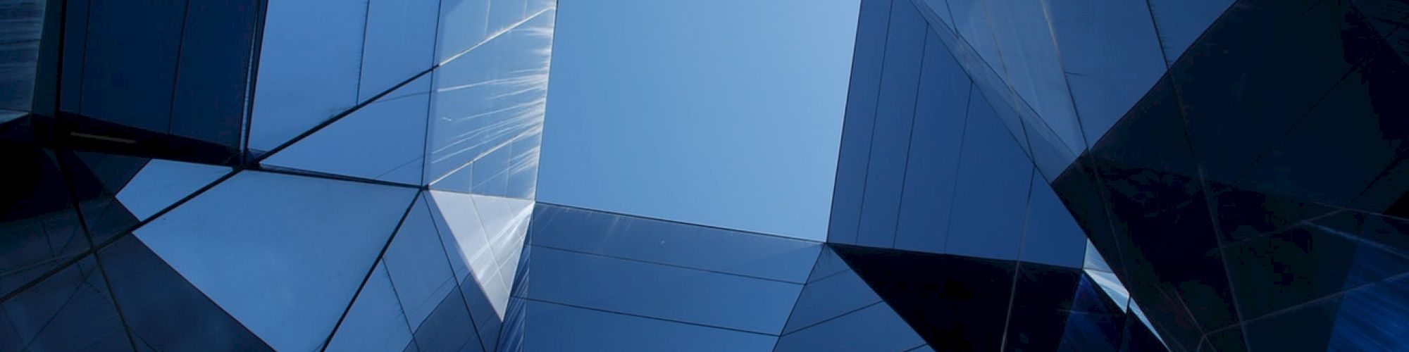 Abstract architecture view looking upward at mirrored surfaces converging at a blue sky opening.