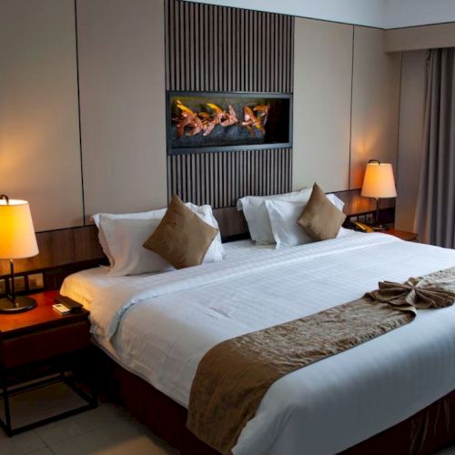 A cozy hotel room with a large bed, two bedside lamps, and decorative cushions, creating a warm and inviting atmosphere.
