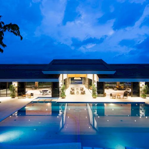 A modern building with a large illuminated pool in front, set against a twilight sky, creating a serene and luxurious ambiance.