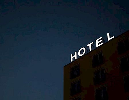 A building with illuminated letters spelling "HOTEL" on the top, set against a dark sky, partially visible in the image.