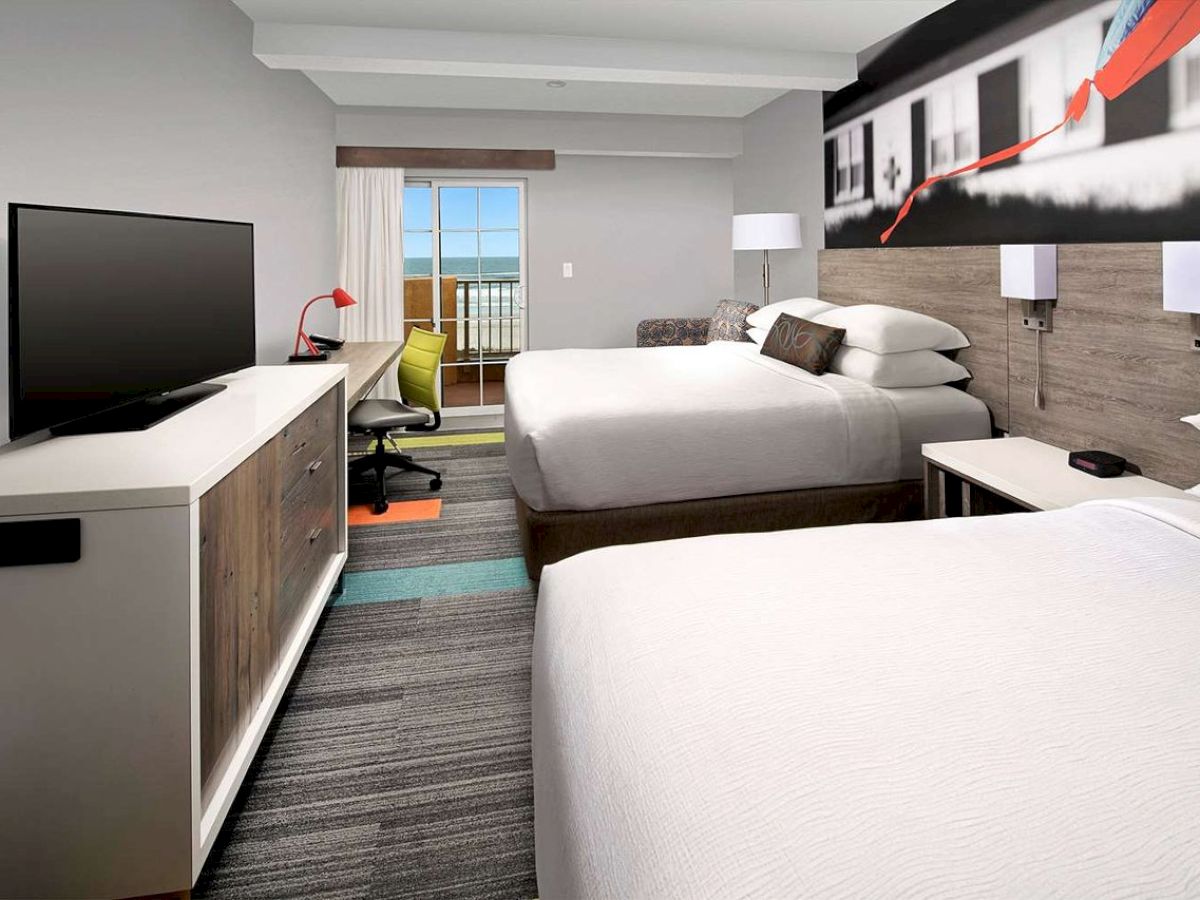 The image shows a hotel room with two beds, a TV, a desk, and a balcony view.