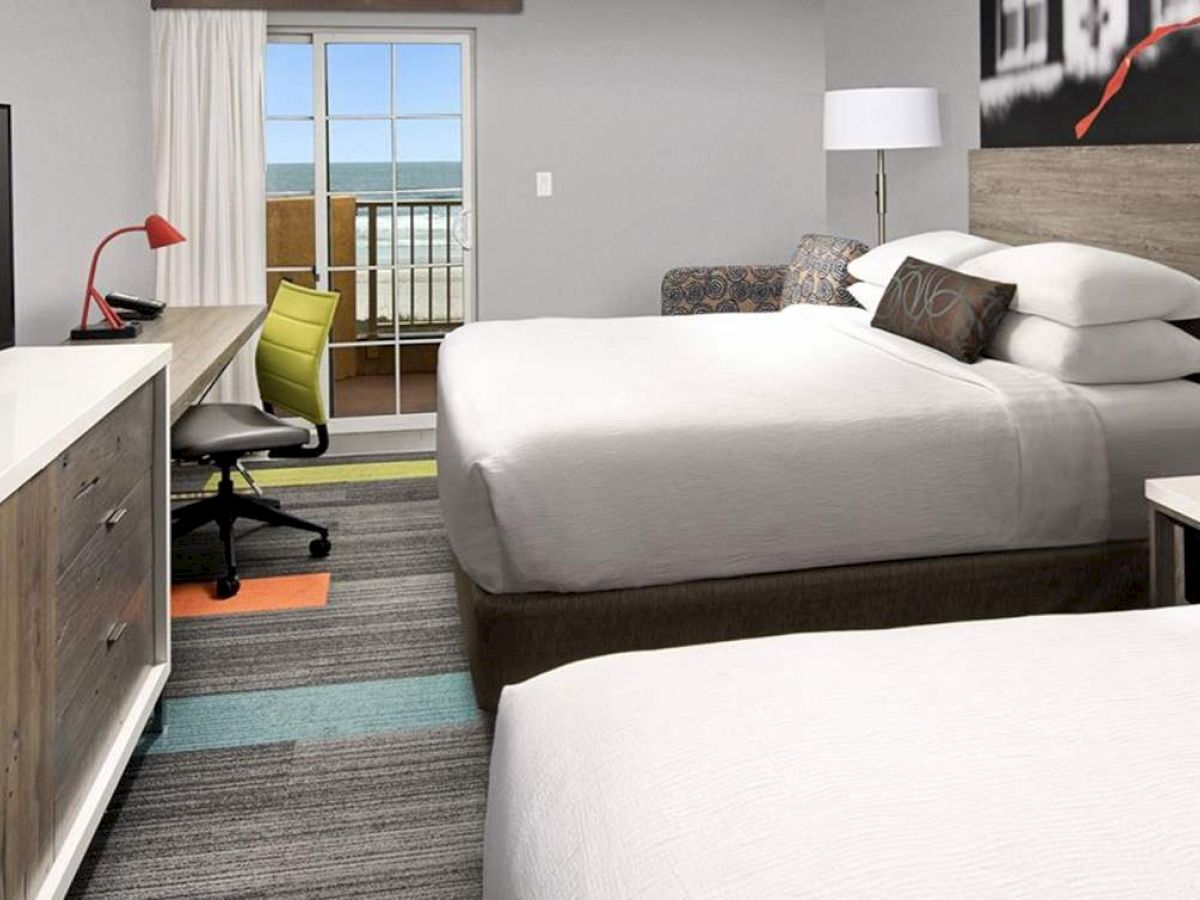 The image shows a hotel room with two beds, a TV, a desk with a chair, and a window with a view.