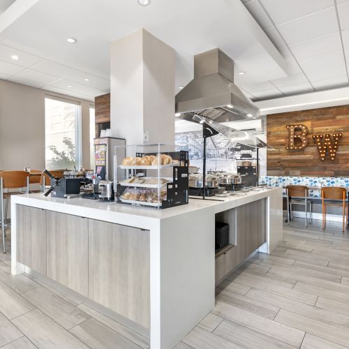 A modern cafe with a clean, stylish interior featuring tables, chairs, and a variety of food items on display near a counter.