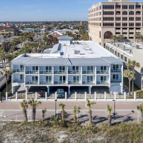 The image shows buildings near a beach, with palm trees lining the street and a clear day in the background.
