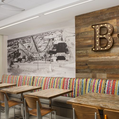 This image shows a cafe interior with colorful seating, wooden tables, a wall photo, and a sign with lit-up letters "BW."