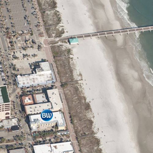 The image shows an aerial view of a coastal area with a beach, buildings, and a pier extending into the ocean.