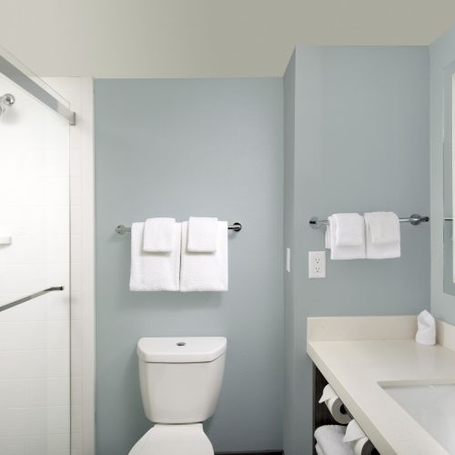 A clean bathroom with a shower, toilet, and sink area, featuring white towels, a mirror, and minimalistic design elements.