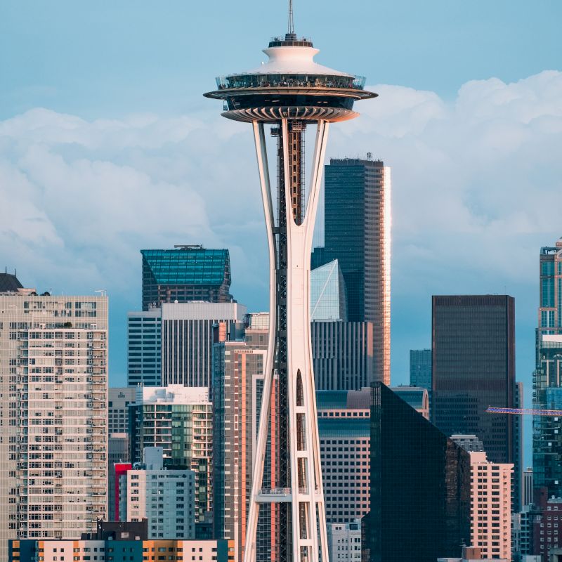 The image shows the Space Needle with a backdrop of city skyscrapers and a partly cloudy sky.