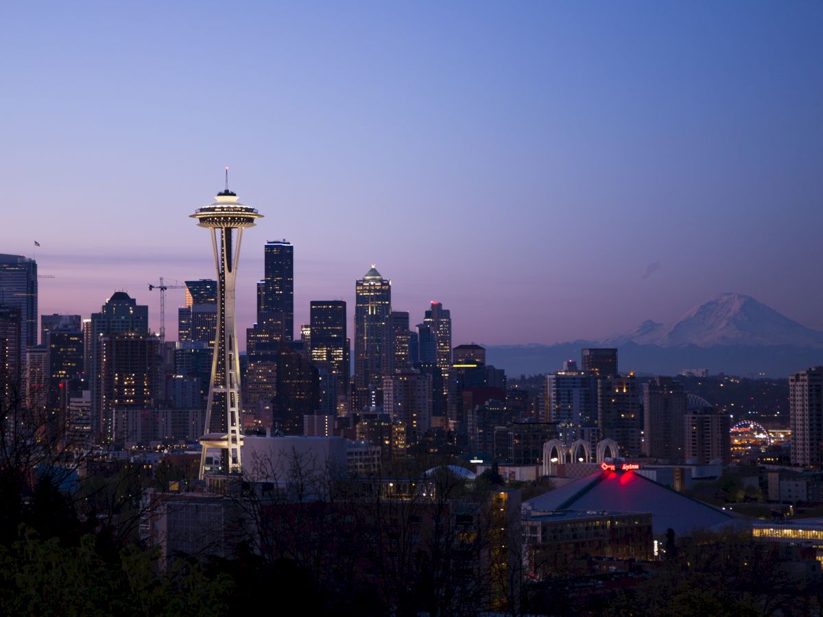 The image shows the Seattle skyline at dusk, with the Space Needle prominently visible and a mountain in the background.